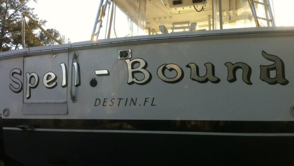 Marine vinyl boat wrap with custom “Spell Bound” lettering and Destin, FL text on a sleek boat hull, showing clean typography and professional wrap design.