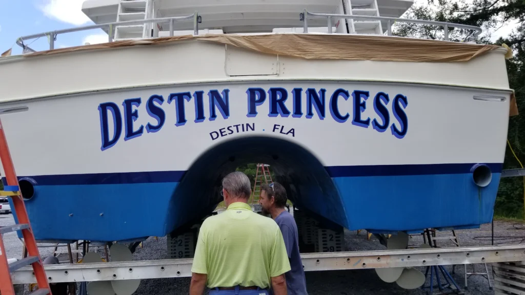 Two men inspecting the blue and white Destin Princess boat with custom transom lettering and marine graphics.