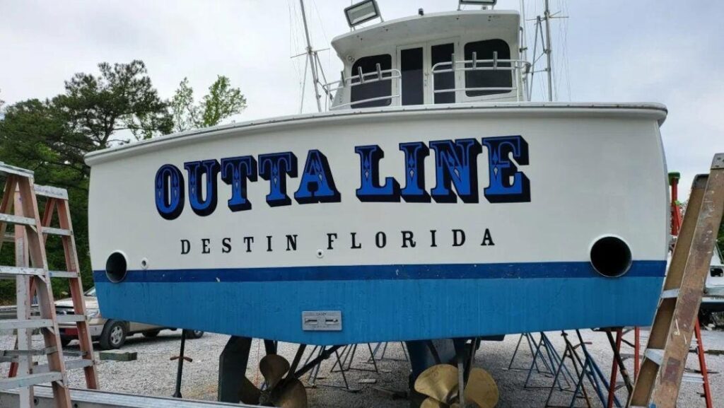 Outta Line, a large fishing vessel with twin propellers, docked in Destin, Florida, featuring its name in bold blue lettering on the stern.